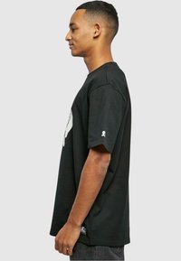 Sort bomulds t-shirt med grafisk print på forsiden, korte ærmer og et lille logo ved nederste kant. Regular fit design.