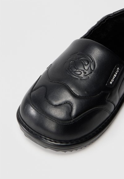Crne kožne cipele na slip-on s podignutim logom, valovitom šavskom dizajnom, zaobljenim vrhom i debelim teksturiranim đonom.