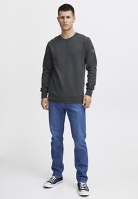 Donkergrijze sweatshirt met lange mouwen, ronde halslijn en geribbelde manchetten, gecombineerd met blauwe jeans en zwart-witte sneakers.