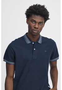 Marineblå polo t-shirt lavet af bomuld, med en krave med en stripet accent. Tre-knaps lukning og korte ærmer med kontrastkant.