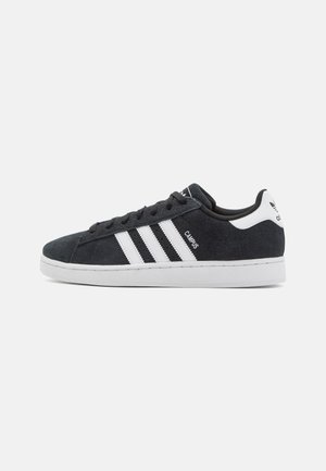 Svart semsket sneakers med hvite striper og merkevare. Har lav profil, rund tå, og hvit gummi såle. Laget for uformelt bruk.