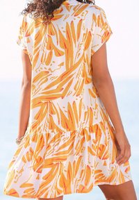 Kurzes ärmelloses Kleid aus weißem Stoff, mit einem lebhaften Muster aus gelben und oranges Blättern, rüschengesäumt und mit einer entspannten Passform.