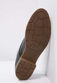 Semelle de chaussure en cuir noir avec un fond en caoutchouc texturé. Présente un motif circulaire et la taille '39' embossée sur le côté.