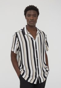 Camicetta a maniche corte con strisce verticali nere, bianche e beige, dotata di un colletto rilassato e una chiusura frontale con bottoni, realizzata in tessuto leggero.