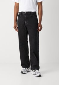 Sorte denimjeans med afslappet pasform, fem-lomme design og metalknapdetaljer. Matchet med en hvid t-shirt og grå sneakers.