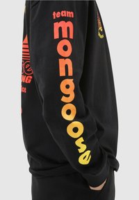 Svart långärmad sweatshirt med djärv orange och gul grafisk text på ärmarna och fram, tillverkad av bomullstyg med en avslappnad passform.