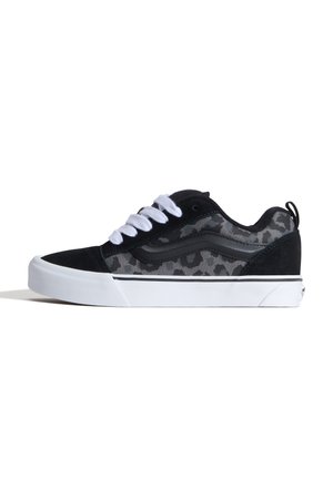 Zapatilla deportiva de caña baja con estampado de leopardo negro y gris, cordones blancos y suela gruesa de goma blanca sobre fondo blanco.