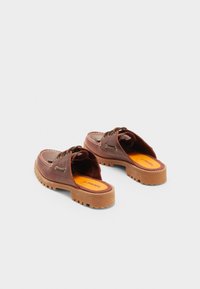 Zapatos de cuero marrón tipo slip-on con parte trasera abierta, suela de goma gruesa, plantilla naranja y costuras decorativas. Punta redonda y detalles de cordones.