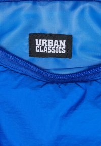 Tessuto blu con un interno testurizzato, caratterizzato da un'etichetta nera con la scritta "URBAN CLASSICS" in bianco. Cerniera lungo il bordo.