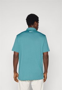 Πόλο μπλούza σε τυρκουάζ απόχρωση με κοντά μανίκια και υφασμάτινο σχέδιο, με λευ�κό λογότυπο Nike στην πίσω κολάρο. Σχεδιασμένο για καθημερινή χρήση.
