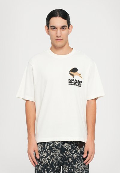 T-shirt in cotone color crema con maniche corte, decorata con una grafica pixelata e la scritta "FOTO NUDES PROIBITE" nella zona sinistra del petto.