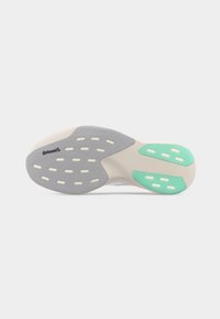 Σόλα παπουτσιού με γκρι και τιρκουάζ λαστιχένιες επιφάνειες πρόσφυσης και ορθογώνιες εγκοπές σε λευκή ενδιάμεση σόλα, με απλό φωτεινό φόντο.