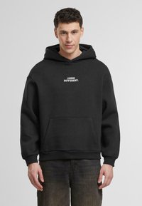 Sudadera negra con un bolsillo canguro, que presenta el texto en blanco "PIENSO DIFERENTE." en el pecho. Hecha de algodón, con tejido texturizado.