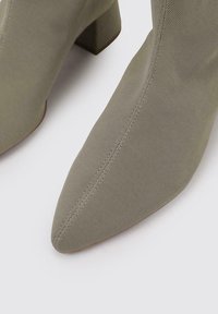 Bottines en tissu texturé vert avec un bout pointu et un talon épais. Couture détaillée sur les côtés et doublure intérieure lisse.