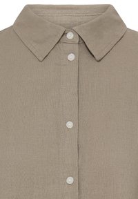 Chemise beige à col avec boutons visibles sur le devant et tissu texturé, vue en gros plan.