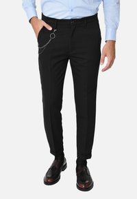 Pantaloni neri su misura con un accento a catena, caratterizzati da una vestibilità slim, una texture liscia e tasche laterali. Abbinati a scarpe scure lucide.