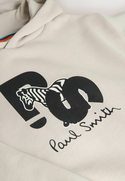 Tissu beige avec de grandes lettres noires "PS", un zèbre intégré à la lettre "S", et "Paul Smith" écrit en dessous en cursive.