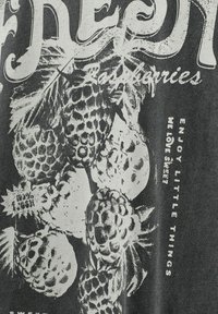 T-shirt grigio scuro con una grafica bianca di piante di ananas con foglie sovrapposte e testo che recita "Goditi le piccole cose."