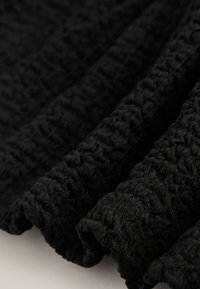 Detail černé texturované látky se svraštělými sklady a mírně lesklým povrchem.