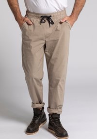 Beige katoenen broeken met een elastische taille en koord, met zijzakken en opgerolde manchetten, gecombineerd met zwarte veterschoenen.
