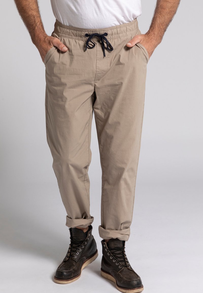 Beige katoenen broeken met een elastische taille en koord, met zijzakken en opgerolde manchetten, gecombineerd met zwarte veterschoenen.