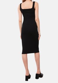 Robe moulante noire côtelée avec encolure carrée et bretelles, silhouette ajustée, longueur au genou, assortie à des chaussures à talons épais.