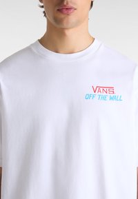 Weißes Baumwoll-T-Shirt mit Rundhalsausschnitt und kurzen Ärmeln. Roter und blauer "VANS OFF THE WALL" Text-Logo auf der Brust.