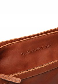 Borsa in pelle marrone scuro con una superficie liscia, caratterizzata da un nome del marchio impresso, una chiusura con cerniera e un bordo cucito lungo il margine.
