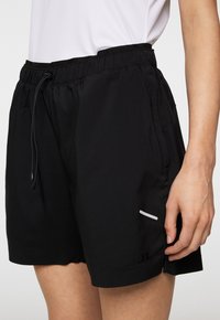 Svarta träningsshorts med elastiskt midjeband och dragsko. Har sidofickor och en reflektörsdetalj på fållen. Slät textur.