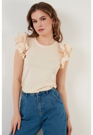 Haut beige clair avec des manches courtes à volants, un col rond et un tissu doux. Associé à un jean en denim bleu taille haute.