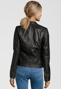 Schwarze Lederjacke mit enger Passform, glatter Textur und strukturierten Schultern. Getragen mit blauen Jeans, die einen lässigen Stil präsentieren.