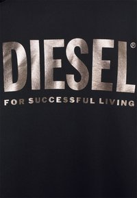 T-shirt in tessuto nero con stampa metallica argento: "DIESEL" in lettere maiuscole e in grassetto, e "FOR SUCCESSFUL LIVING" sotto, in carattere più piccolo.
