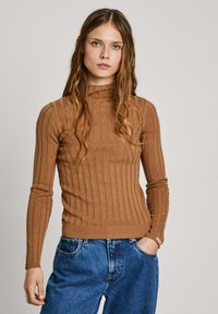 Brun randig polotröja med lång ärm, figurnära siluett och ribbad nederkant. Matchad med löst sittande blå denimjeans.