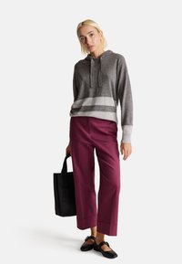 Šedá pletená mikina s bílými pruhy, spárovaná s vínovými kalhotami s širokými nohavicemi. Černá taška a černé baleríny dokončují kompletní vzhled.