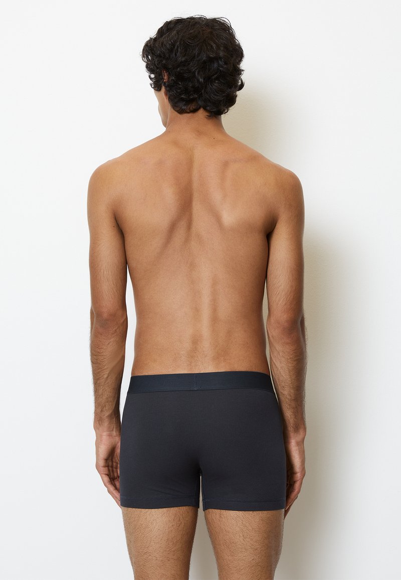 Boxers ajustés à côtes gris foncé avec une taille élastique, vus de dos. Le tissu semble légèrement texturé et ajusté.
