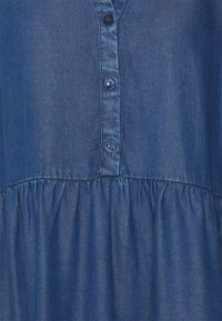 Vestido de mezclilla azul con una placket de botones, cintura fruncida y una textura suave. Presenta un cuello clásico y un dobladillo redondeado.