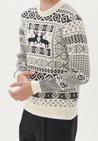Pull en maille crème avec motifs bleu marine, présentant des dessins géométriques et de cerfs, col rond et poignets côtelés.