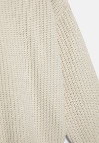 Pulover tricotat de culoare crem, cu un design texturat, cu dungi și umeri căzuți, evidențiind detalii intricate și moliciune.