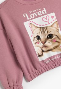 Sudadera rosa con ribete elástico, que presenta una imagen impresa de un gato rodeado de corazones y un texto que dice "Es hora de ser amado."