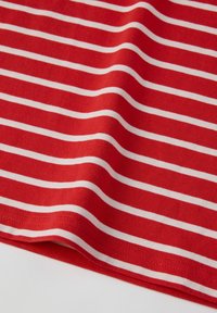 Punainen puuvillakangas, jossa on vaakasuoria valkoisia viivoja, jolla on sileä rakenne ja ommeltu helma, luoden tasaisen kuvion pinnalle.