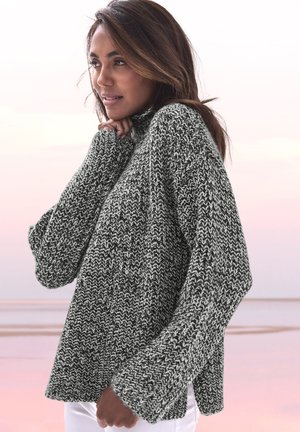 Grober Strickpullover in Schwarz und Weiß, mit hohem Kragen, weiten Ärmeln und lockerer Passform sowie einem strukturierten Muster.