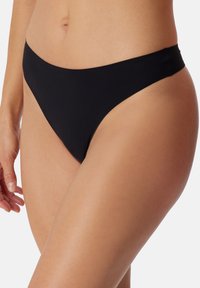 Bas de bikini noir en tissu extensible, présentant un design taille basse et une couverture minimale. Texture lisse sans motifs visibles.