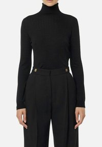 Maglione nero a coste con collo alto in un design aderente, abbinato a pantaloni neri a vita alta. I pantaloni presentano dettagli dorati sulla cintura.