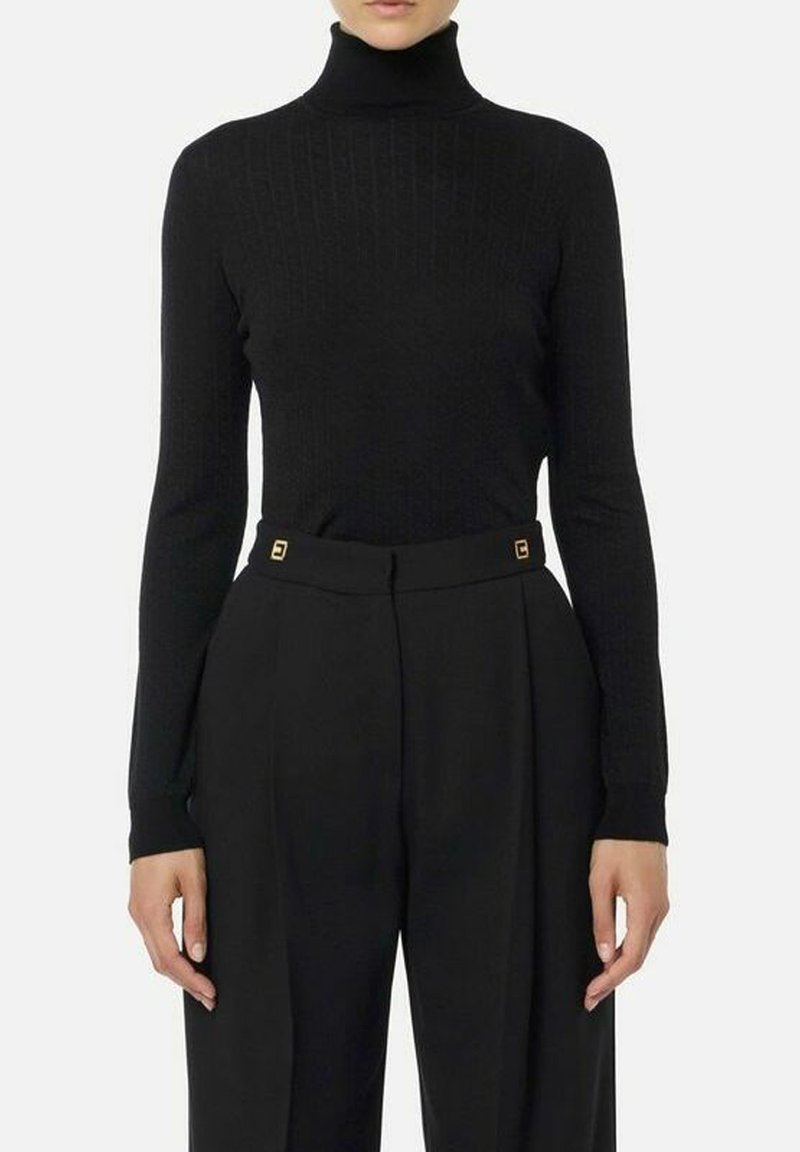 Maglione nero a coste con collo alto in un design aderente, abbinato a pantaloni neri a vita alta. I pantaloni presentano dettagli dorati sulla cintura.