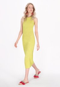 Stickad, ärmlös, ljusgul klänning med en figurnära silhuett och midi längd. Bärs med rosa sandlever med röda tofsar.