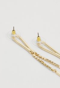 Boucles d'oreilles en or avec un design en chaîne, dotées de fermoirs transparents et de détails complexes le long des maillons, créant un mélange de textures et de formes.