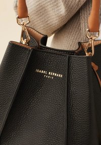 Black pebbled leather handbag featuring golden logo "ISABEL BERNARD PARIS," with tan leather straps and a textured finish.