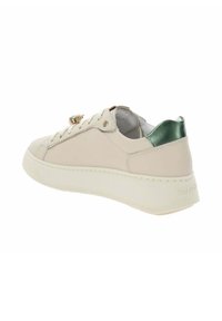 Beige lage sneaker met dikke witte zool, groene metallic hielkap, vetersluiting aan de voorkant en een decoratief gouden embleem op de tong.