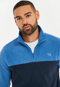 Halb-Reißverschluss Fleece-Pullover in Hellblau und Marineblau. Weicher Stoff mit einem Reißverschluss, Logo auf der linken Brust und Design mit kontrastierenden Farben.