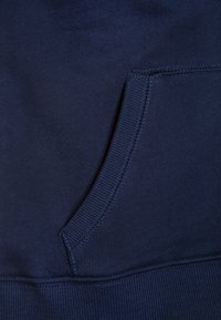 Un sweat-shirt bleu marine en tissu avec une poche kangourou aux bords côtelés, une texture douce et des détails de couture serrée le long des coutures.